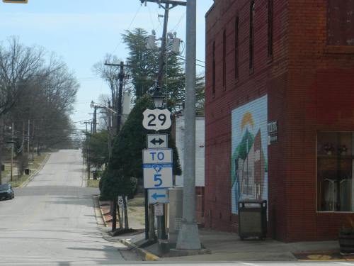 A street view showing a sign for Route 29 and a directional sign pointing to Route 5, with a brick building nearby.