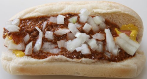 A hot dog in a bun topped with chili and diced onions.