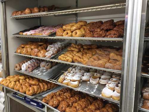 A display of various donuts, including glazed, sprinkled, and powdered varieties, arranged on shelves.