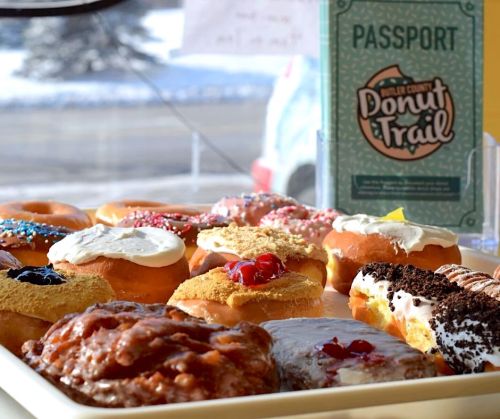 A variety of colorful donuts with toppings displayed in a case, alongside a "Donut Trail" passport.