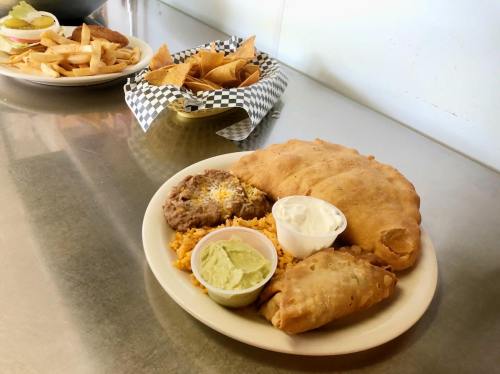 A plate of food featuring a large calzone, rice, beans, sour cream, guacamole, and a smaller fried item.