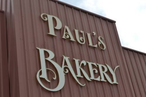 Sign for "Paul's Bakery" in elegant lettering on a brown metal building.