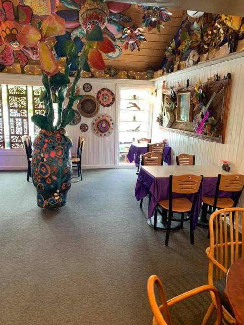 Colorful restaurant interior with vibrant decor, purple tablecloths, and unique wall art. Cozy dining area with plants.