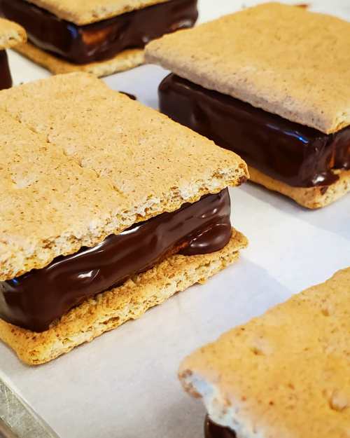 Close-up of graham cracker sandwiches filled with chocolate, resting on parchment paper.