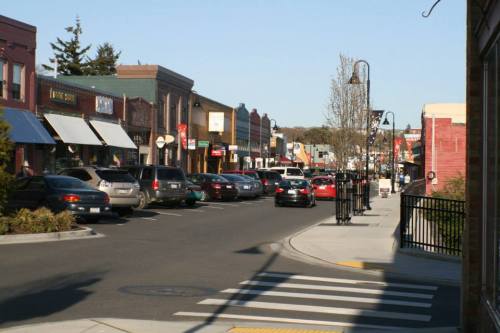 A charming street lined with shops and parked cars, featuring trees and a clear blue sky.