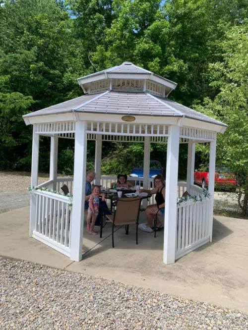 A family enjoys a meal together in a gazebo surrounded by greenery.