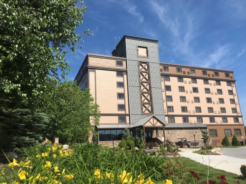 A modern hotel building surrounded by greenery and colorful flowers under a clear blue sky.