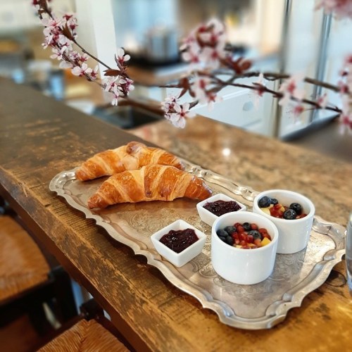 A silver tray with croissants and small bowls of fruit and jam, set against a backdrop of cherry blossoms.