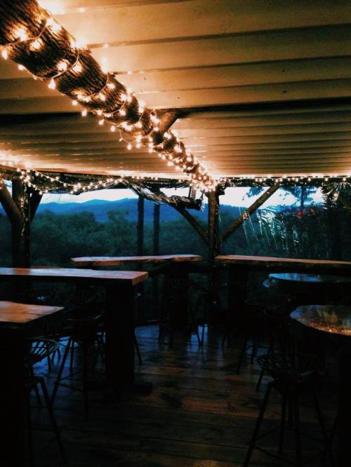 Cozy interior with wooden tables, string lights, and a view of mountains at dusk.