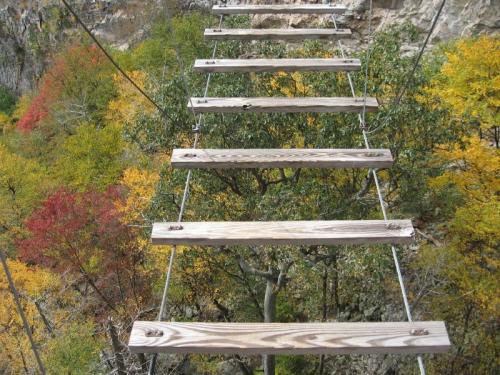 A wooden suspension bridge with planks over a colorful autumn forest.