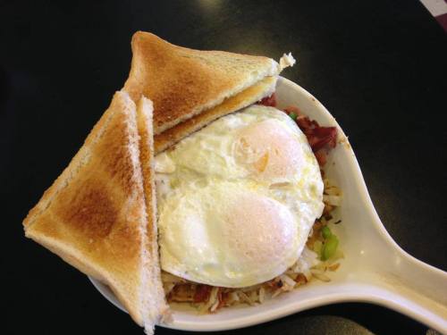 A bowl of fried rice topped with two sunny-side-up eggs, accompanied by two slices of toasted bread.