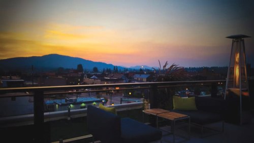 A serene sunset view from a rooftop, with mountains in the background and cozy seating in the foreground.