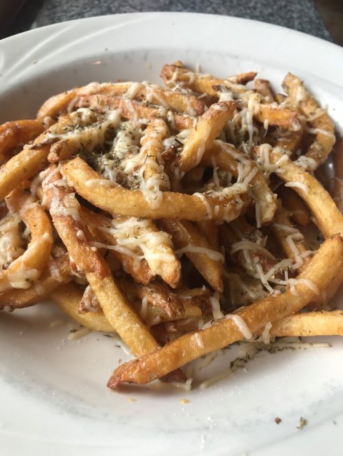 A plate of golden-brown French fries topped with melted cheese and herbs.