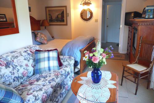 Cozy room featuring a floral sofa, a bed, a wooden dresser, and a table with a vase of flowers.