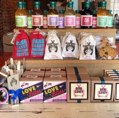 A display of colorful candy products, including bags of toffee, cookies, and drinks, arranged on a wooden counter.