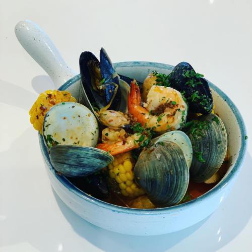 A bowl of seafood featuring shrimp, clams, mussels, and corn, garnished with herbs.