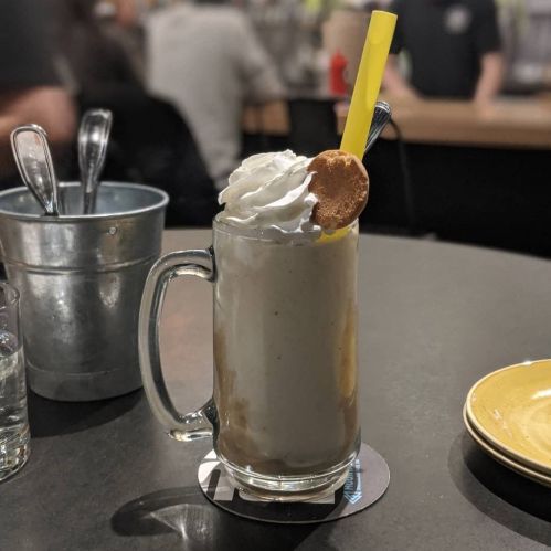 A frosty mug filled with a creamy drink topped with whipped cream and a cookie, served with a yellow straw.