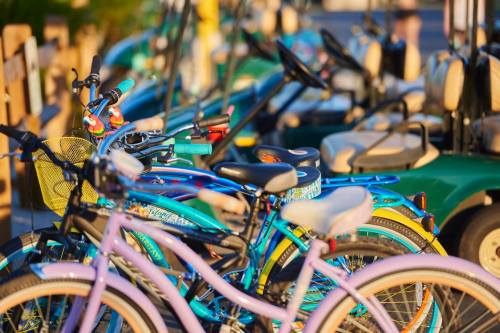 A row of colorful bicycles parked alongside green golf carts in a sunny outdoor setting.