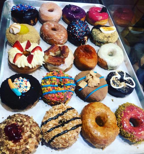 A variety of colorful donuts displayed on a tray, featuring toppings like sprinkles, fruit, and chocolate.