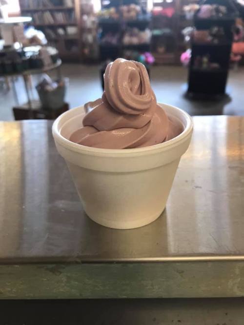 A swirl of chocolate soft serve ice cream in a small white cup, placed on a metal surface.