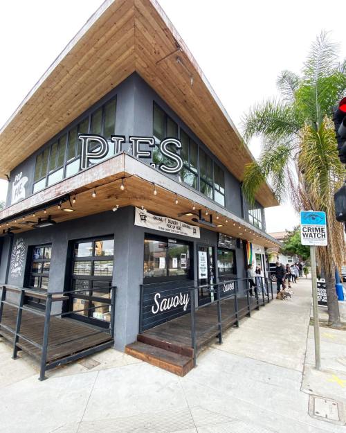 A corner building with a sign reading "Pies" and "Savory," featuring outdoor seating and palm trees nearby.