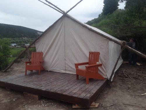 A canvas tent on a wooden platform with two red Adirondack chairs in front, set in a natural outdoor environment.