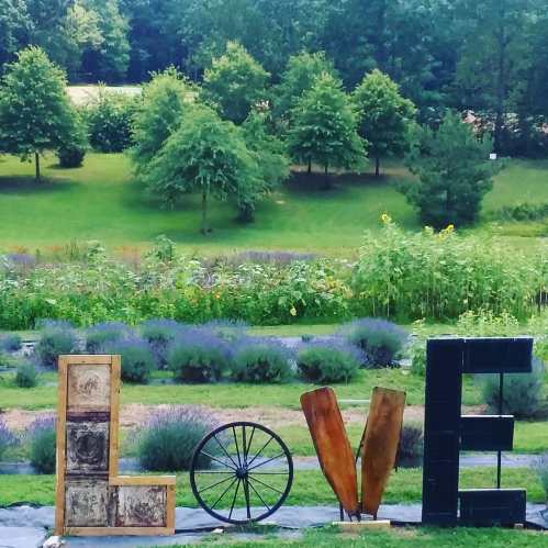 A creative outdoor display spelling "LOVE" with wooden letters, a wheel, and greenery in the background.