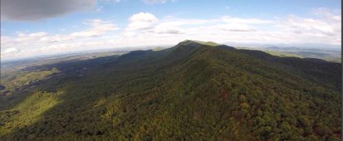Aerial view of a lush, green mountain range under a partly cloudy sky, showcasing rolling hills and valleys.