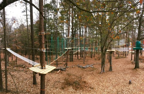 A treetop adventure course with wooden platforms and rope bridges among trees in a wooded area.