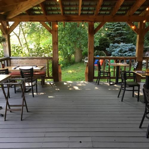 A wooden deck with tables and chairs, surrounded by greenery and string lights, creating a cozy outdoor space.