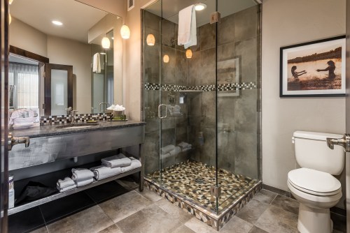 Modern bathroom featuring a glass shower, sink with towels, and a toilet, with stylish tile and lighting.
