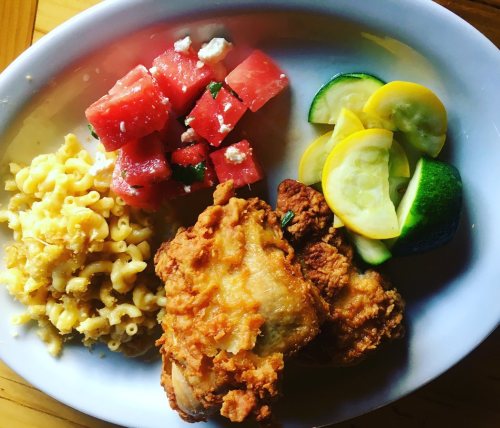 A plate featuring fried chicken, macaroni and cheese, watermelon salad, and sautéed yellow and green squash.