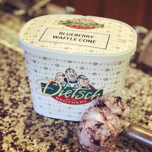 A tub of Dietsch Brothers blueberry waffle cone ice cream with a scoop resting beside it.
