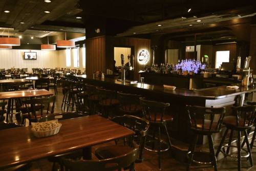 A spacious restaurant interior featuring wooden tables, a bar with illuminated taps, and a cozy atmosphere.