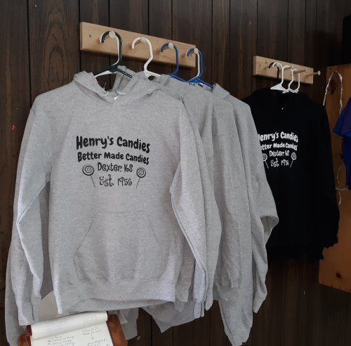 Hoodies hanging on a wall, featuring "Henry's Candies" logo and establishment year, in gray and black colors.