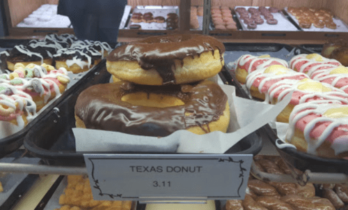 A display of donuts, featuring a large Texas donut topped with chocolate icing, priced at $3.11.