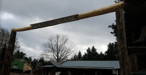 Sign reading "Frenchman's Bend" on a wooden archway, with a cloudy sky and trees in the background.