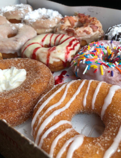 A variety of colorful donuts in a box, featuring sprinkles, icing, and powdered sugar toppings.