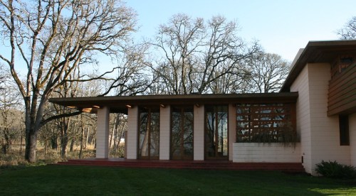 A modern building with large glass windows, surrounded by trees and grass under a clear blue sky.
