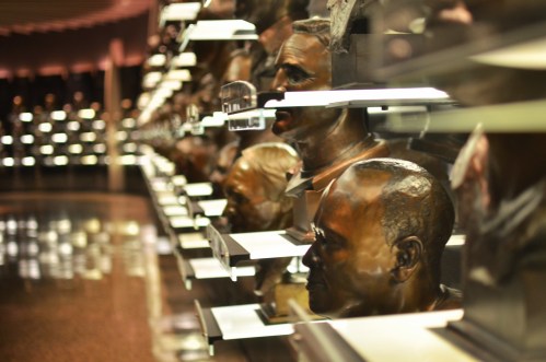 A row of bronze busts displayed on shelves, reflecting light in a dimly lit space.