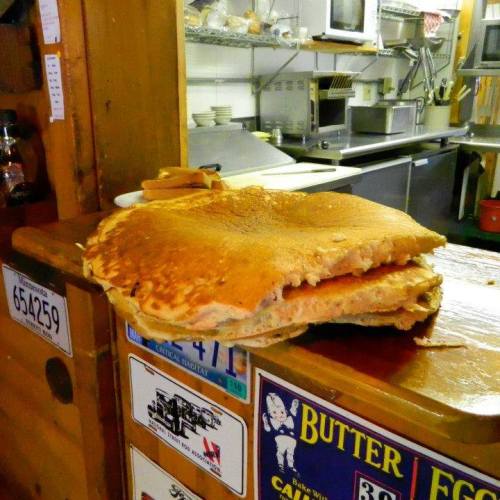 A large, fluffy pancake stacked on a plate, resting on a wooden counter in a cozy kitchen setting.