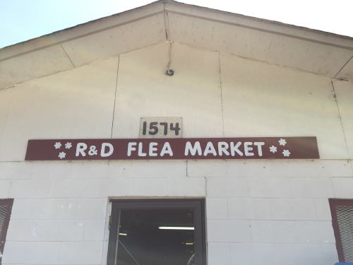 Sign for R&D Flea Market on a white building, with the address 1574 displayed above the entrance.