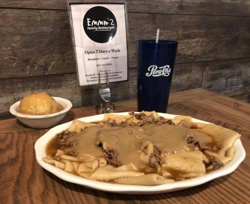 A plate of beef and gravy over noodles, with a side of applesauce and a Pepsi drink on a wooden table.