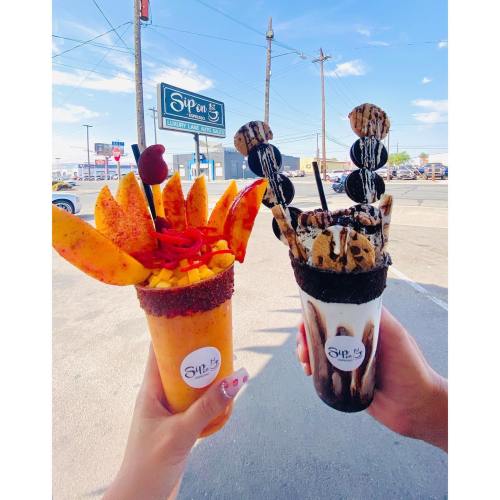 Two colorful dessert cups filled with fruit and toppings, held by hands against a sunny outdoor backdrop.
