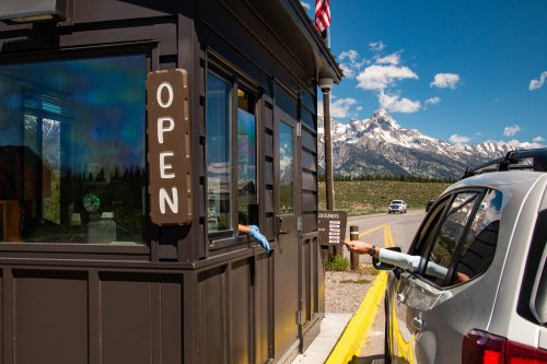 A car at an open park entrance booth with mountains in the background and a clear blue sky.