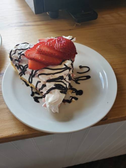 A slice of cake topped with whipped cream, strawberries, and chocolate drizzle on a white plate.