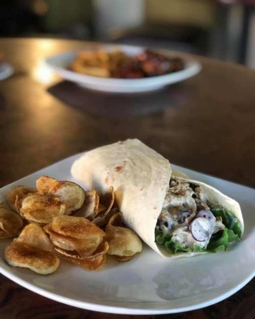 A plate with a wrapped tortilla filled with chicken and lettuce, accompanied by a side of crispy potato chips.