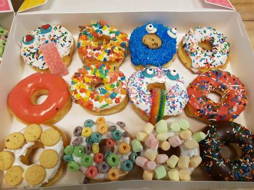 A colorful assortment of decorated donuts in a box, featuring sprinkles, candy, and playful designs.