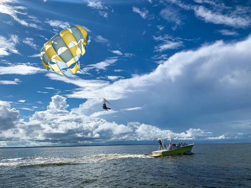 A boat pulls a colorful parachute with two people soaring above the water under a bright blue sky with clouds.