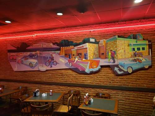 A colorful mural depicting vintage cars and people in a retro diner setting, illuminated by red neon lights.